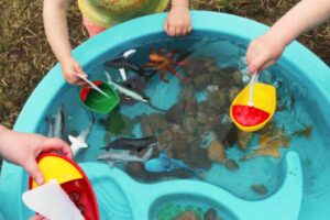 Children playing with toys, rocks and leaves in a water table