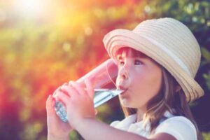 Young girl in straw hat drinking a glass of water