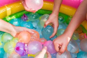 Hands of children reaching for water balloons from big container